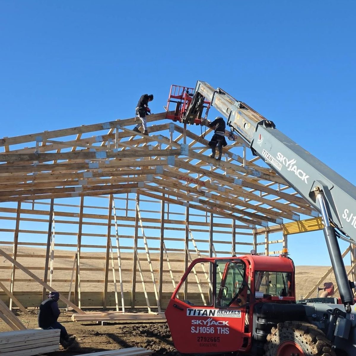 Two crew members setting roof trusses from a telehandler basket