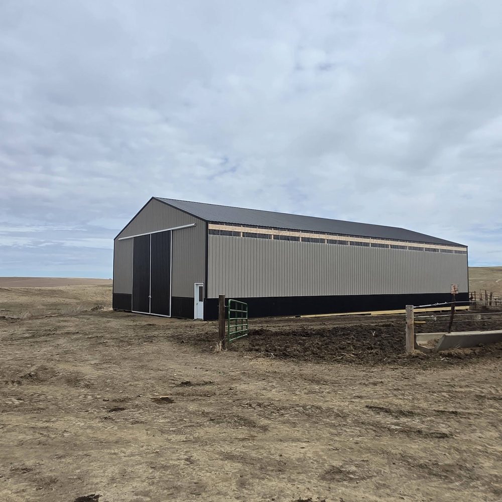 A gray and black post-frame barn on a ranch under an overcast sky