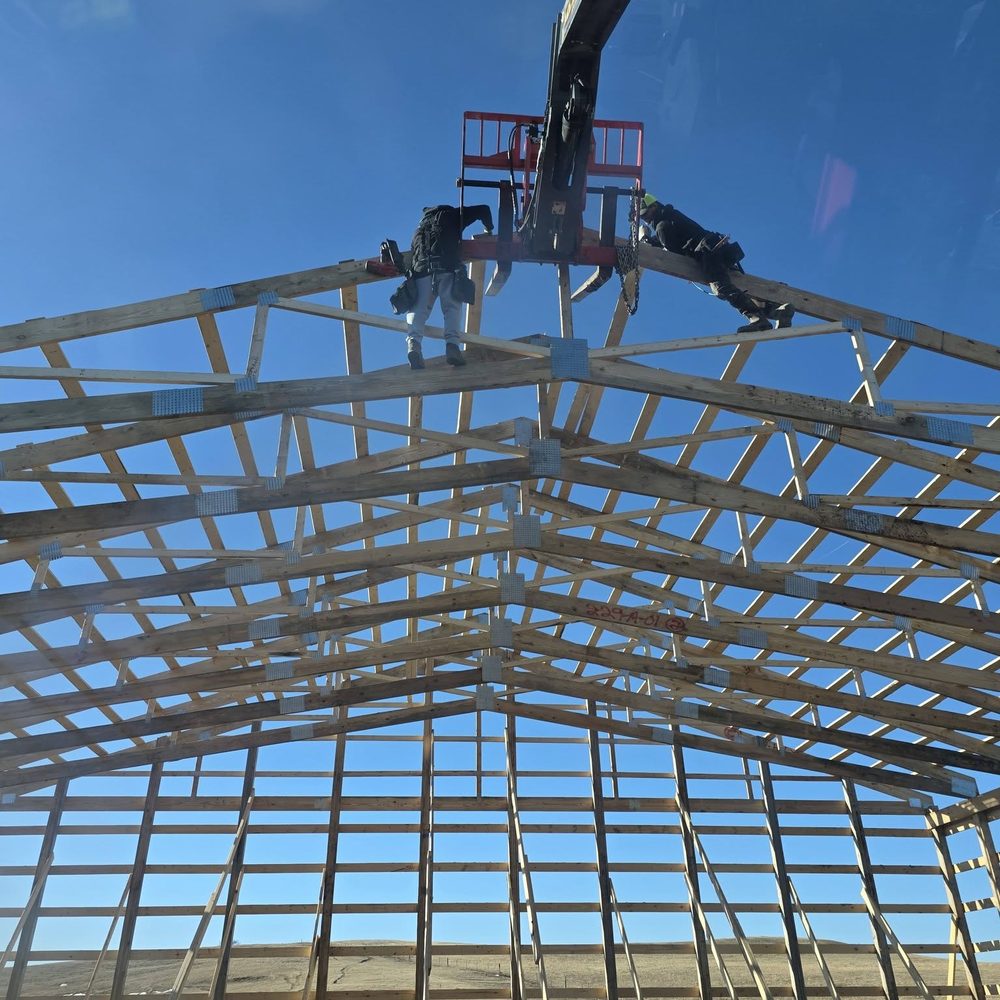 Looking up at a completed post-frame truss roof against a blue sky