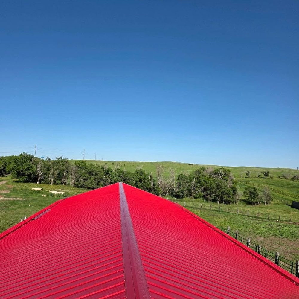 A bright red steel roof above green summer hills
